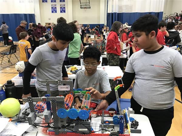 Three students work on their robot at a VEX IQ Robotics competition.